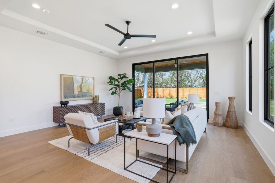 Living room featuring a ceiling fan, light wood-style floors, recessed lighting, and a raised ceiling