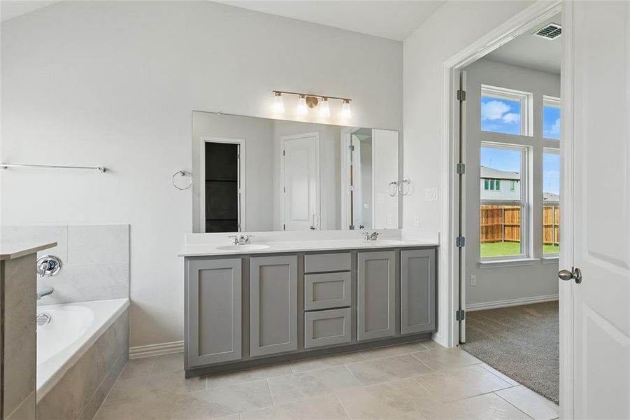 Bathroom with double vanity, a bath, light tile patterned flooring, and light colored carpet