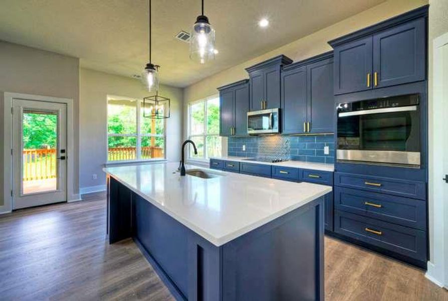A contemporary kitchen features rich blue cabinetry, sleek white countertops, and durable hardwood flooring.