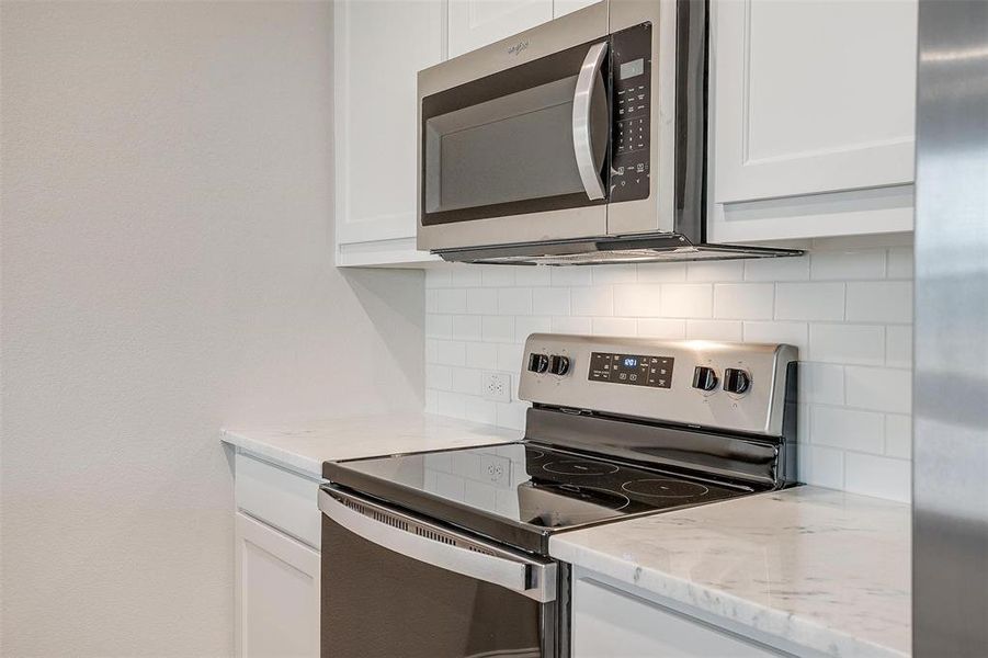 Kitchen with light stone countertops, appliances with stainless steel finishes, and white cabinets