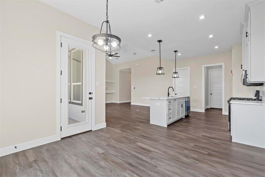 Kitchen featuring hanging light fixtures, dark hardwood / wood-style flooring, sink, white cabinetry, and a kitchen island with sink