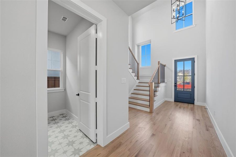 Foyer featuring plenty of natural light, a chandelier, light wood-style flooring, stairway, and a high ceiling