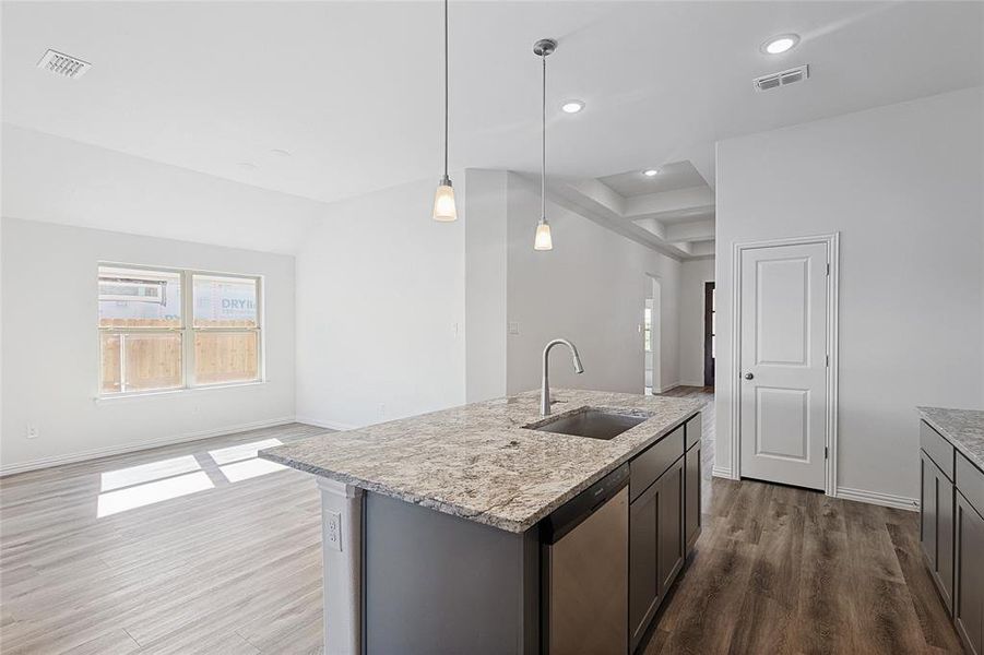 Kitchen featuring pendant lighting, dishwasher, a center island with sink, sink, and hardwood / wood-style flooring