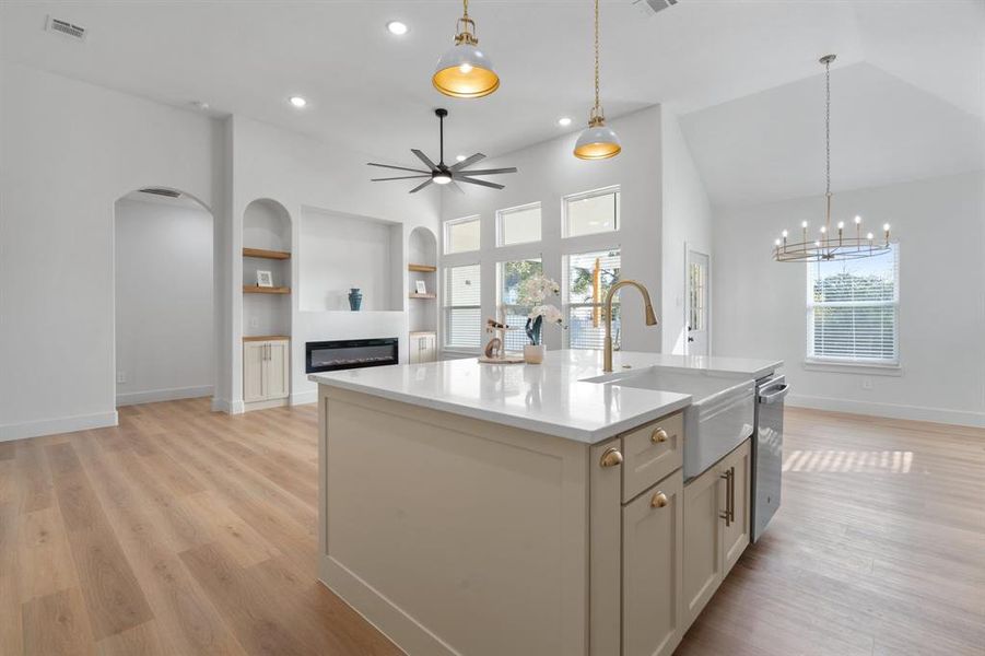 Kitchen featuring ceiling fan, open floor plan, light stone counters, a glass covered fireplace, and an island with sink