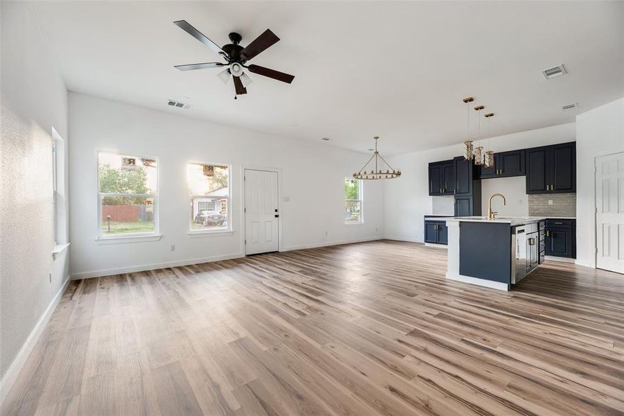 Unfurnished living room featuring suspended lighting, ceiling fan, and light wood finished floors