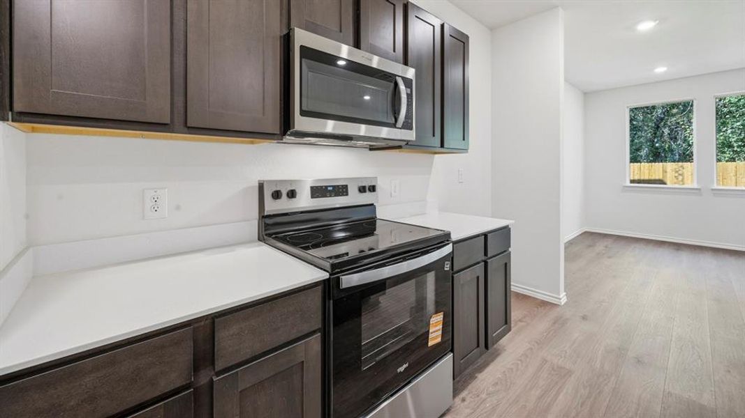 Kitchen with appliances with stainless steel finishes, light wood finished floors, recessed lighting, and dark brown cabinets