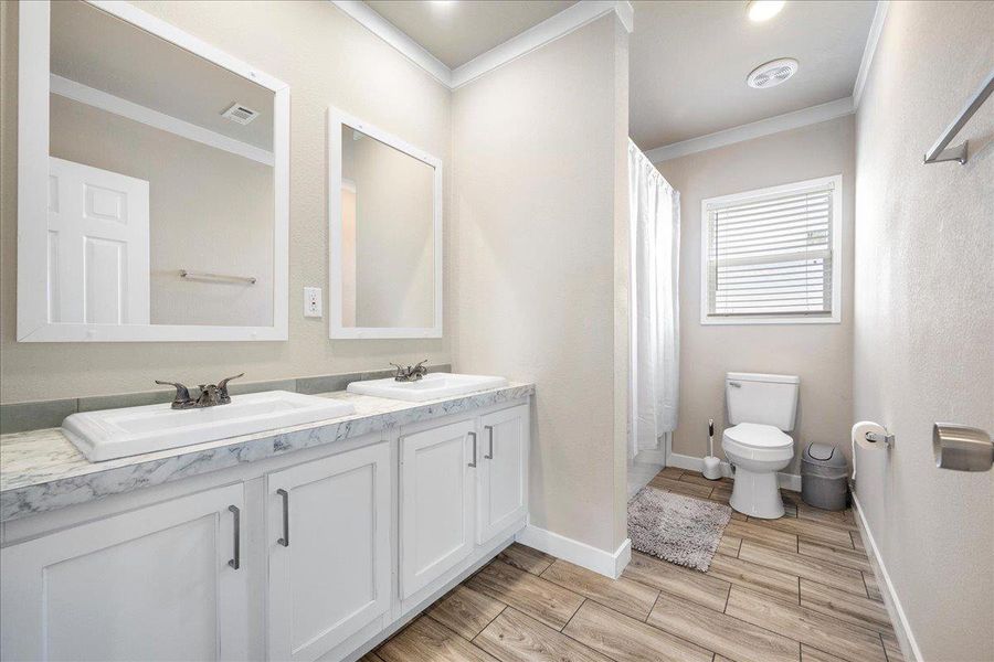 Full bathroom featuring wood finish floors, double vanity, crown molding, and shower / tub combo Full bathroom featuring wood finish floors, double vanity, crown molding, and shower / tub combo