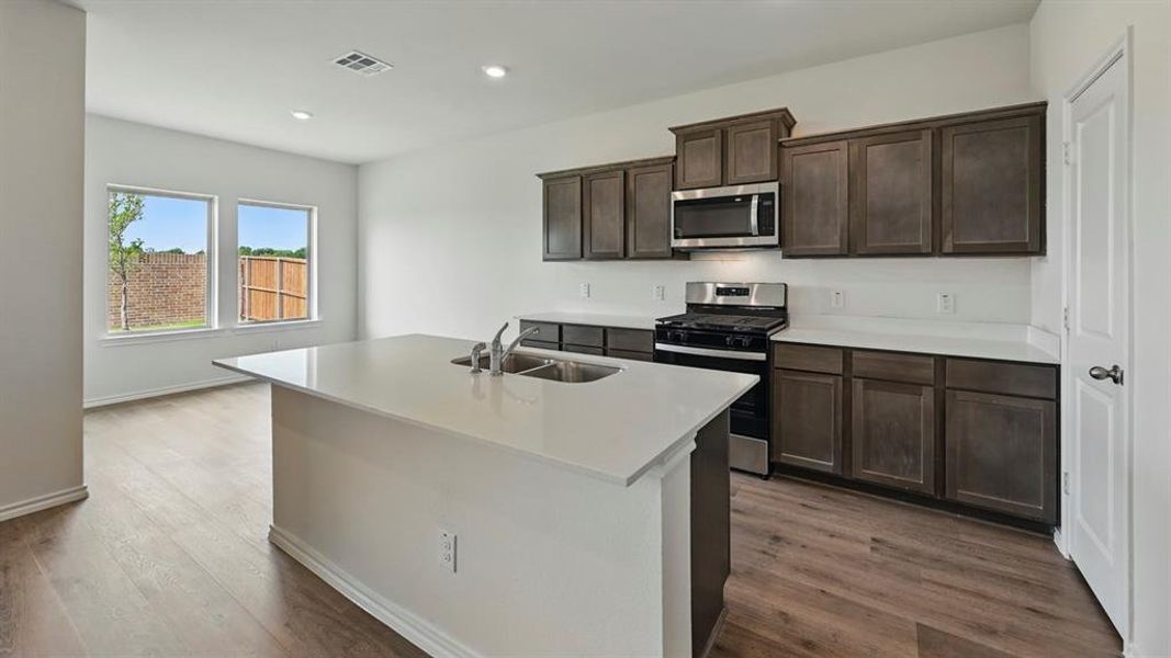 Kitchen with appliances with stainless steel finishes, dark brown cabinets, dark wood-type flooring, recessed lighting, and a center island with sink