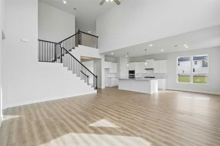 Unfurnished living room featuring a towering ceiling, light wood-type flooring, stairway, baseboards, and recessed lighting Unfurnished living room featuring a towering ceiling, light wood-type flooring, stairway, baseboards, and recessed lighting