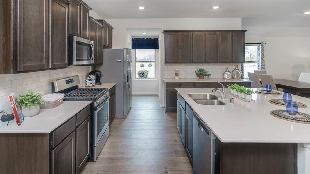 Modern kitchen featuring dark wood-finish cabinetry, light countertops, wood-finish flooring, a stainless steel gas range, and a stainless steel refrigerator