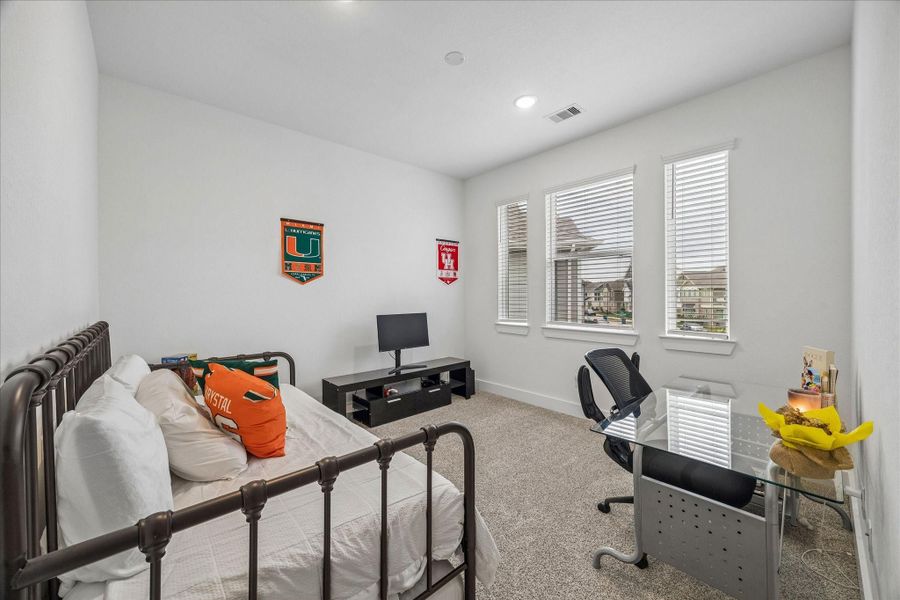 The front-facing secondary bedroom offers plush carpeting, recessed lighting, and abundant natural light from three windows.