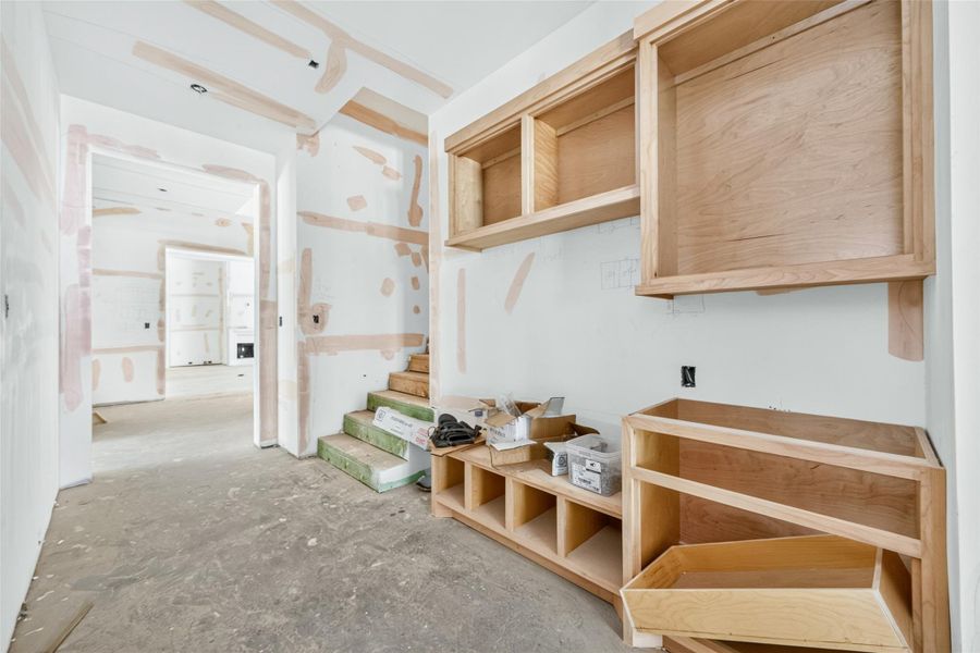 Mud room with a built in bench and stained alder cabinetry leading to the kitchen. Stairs lead to the game room and 5th bedroom