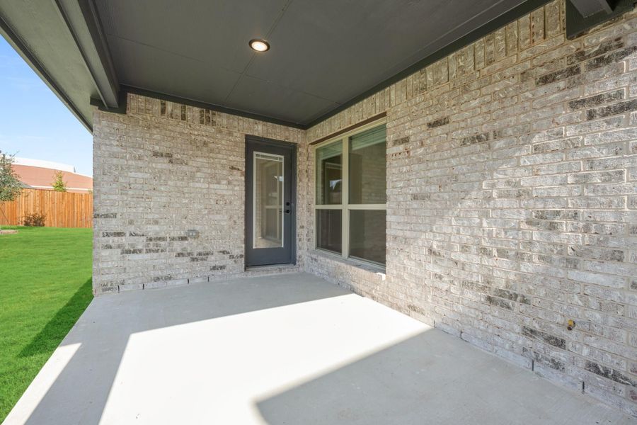 Covered back patio with concrete floor, brick exterior, gray door, and fenced backyard with green lawn