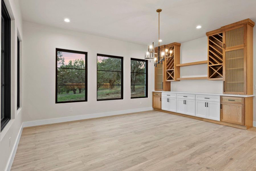 A well-lit dining area features light wood flooring, large windows, and a sophisticated built-in bar with wine storage.