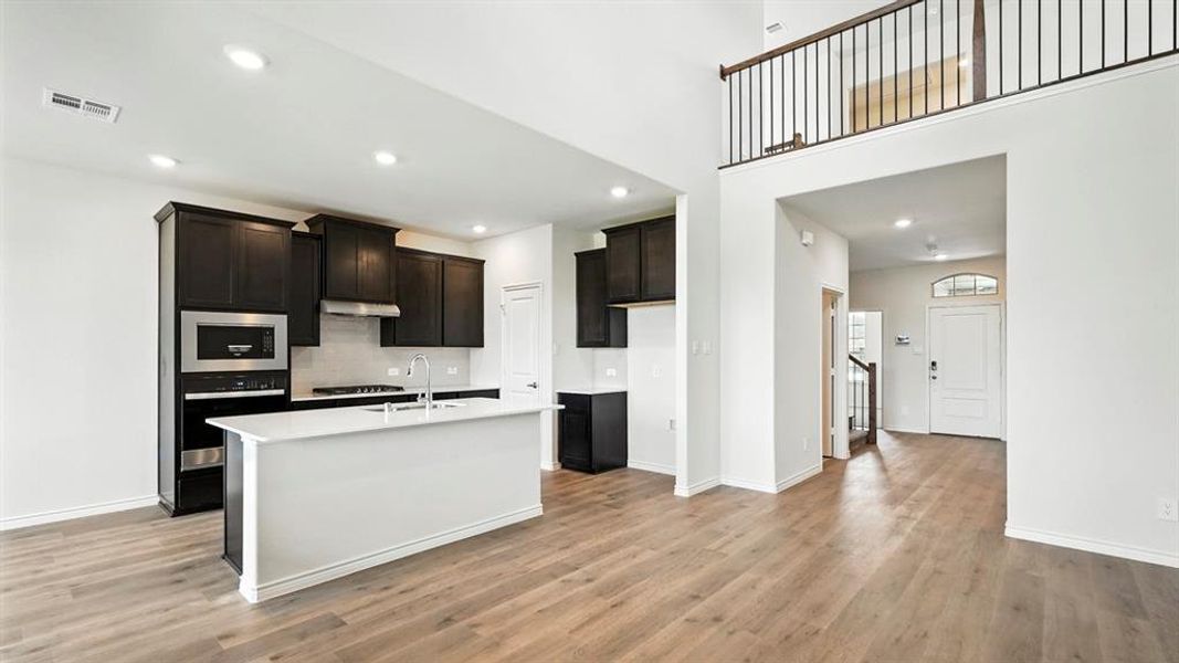 Kitchen featuring stainless steel appliances, a center island with sink, light wood-type flooring, recessed lighting, and light stone counters