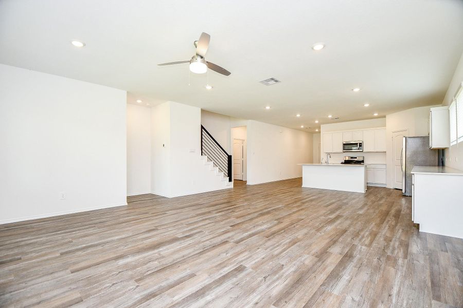 This photo showcases a spacious, open-concept living area with modern wood flooring, recessed lighting, and a ceiling fan. The kitchen features sleek white cabinetry, stainless steel appliances, and an island. A staircase with a contemporary railing leads to the upper level, adding a stylish touch. This photo showcases a spacious, open-concept living area with modern wood flooring, recessed lighting, and a ceiling fan. The kitchen features sleek white cabinetry, stainless steel appliances, and an island. A staircase with a contemporary railing leads to the upper level, adding a stylish touch.