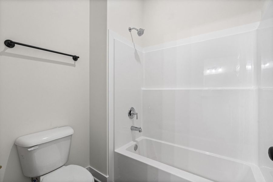 White bathtub and shower combination with chrome fixtures, complemented by a white toilet and a matte black towel bar White bathtub and shower combination with chrome fixtures, complemented by a white toilet and a matte black towel bar