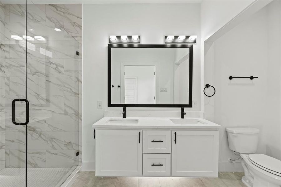 Full bath featuring toilet, double vanity, a marble finish shower, and a sink
