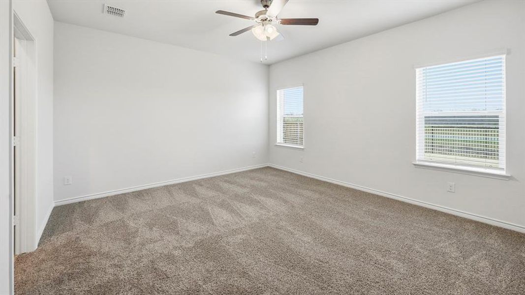 Spacious room featuring neutral carpet flooring, a ceiling fan with light fixture, and two windows with blinds