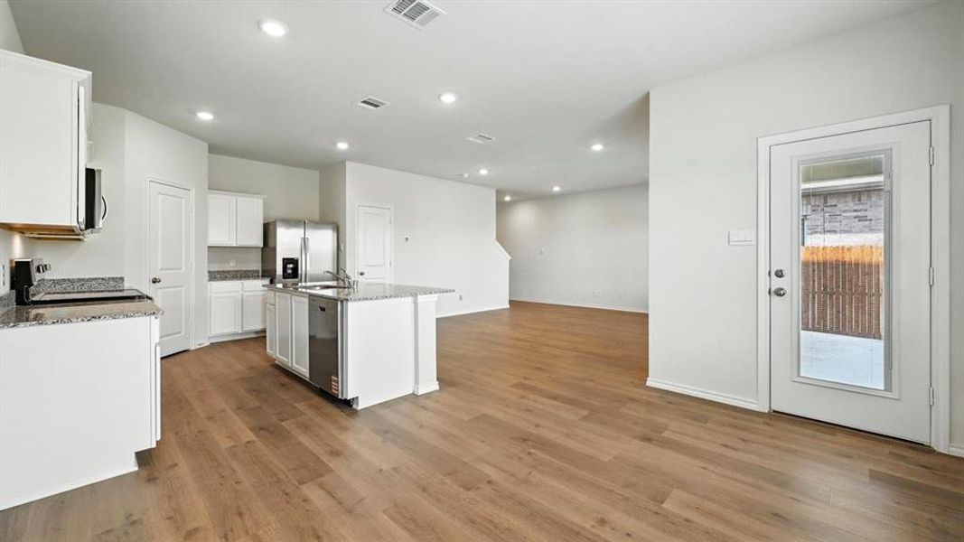 Open-concept kitchen with a central island, white cabinetry, granite countertops, stainless steel appliances, and wood-finish flooring