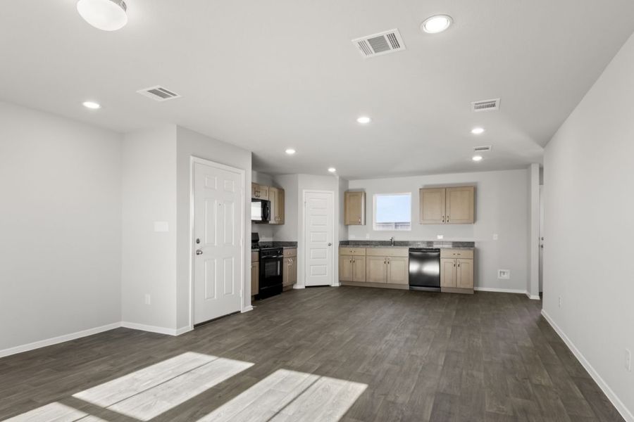Image of a cottage home living room with dark vinyl flooring, light grey walls, and a L-shaped kitchen in the distance Image of a cottage home living room with dark vinyl flooring, light grey walls, and a L-shaped kitchen in the distance