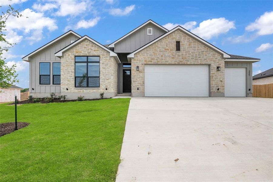 View of front facade featuring a front lawn, stone siding, a garage, board and batten siding, and driveway