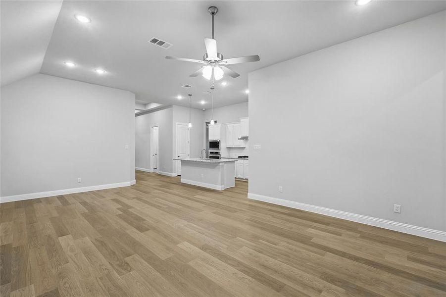 Unfurnished living room with light wood finished floors, a ceiling fan, recessed lighting, and vaulted ceiling Unfurnished living room with light wood finished floors, a ceiling fan, recessed lighting, and vaulted ceiling