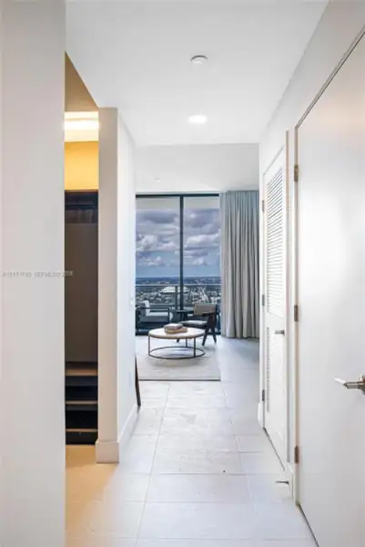 Large-format tile flooring, louvered closet doors, and floor-to-ceiling glass paneling featuring a balcony with an expansive exterior urban landscape