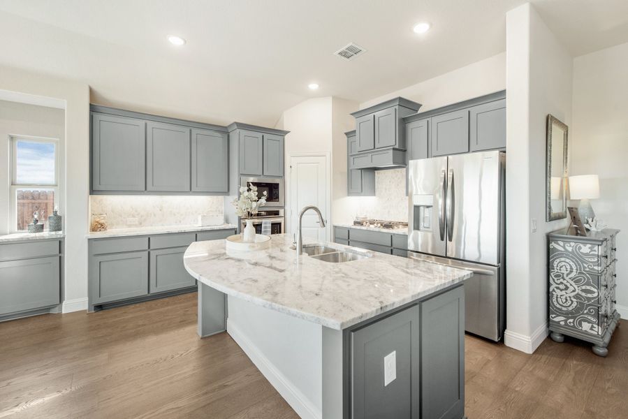Kitchen with gray cabinets, marble island with sink, and stainless steel appliances on hardwood floors
