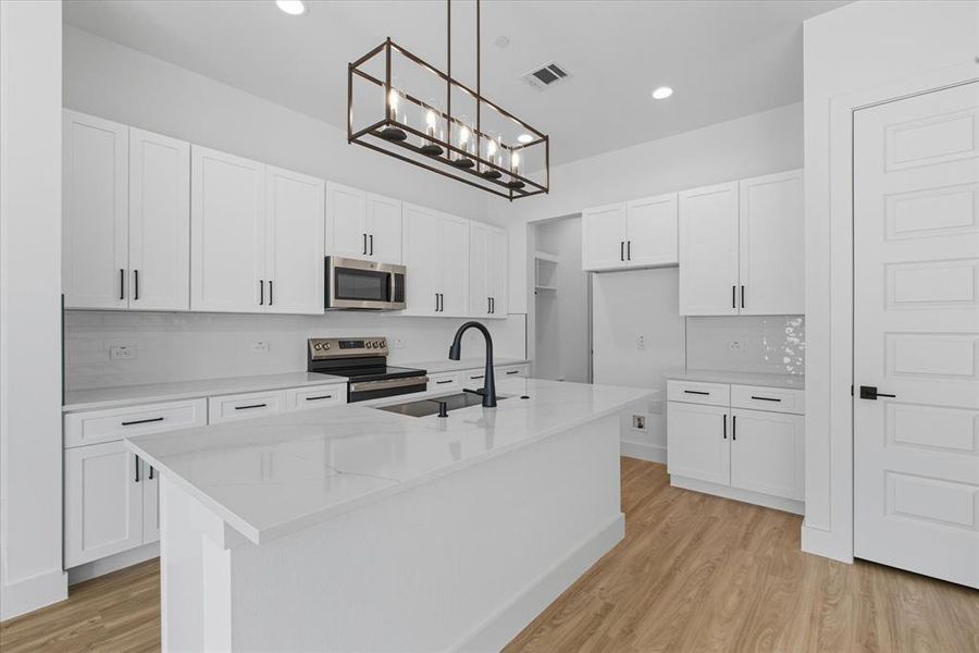 Kitchen featuring decorative backsplash, light wood-style floors, white cabinets, appliances with stainless steel finishes, and a center island with sink