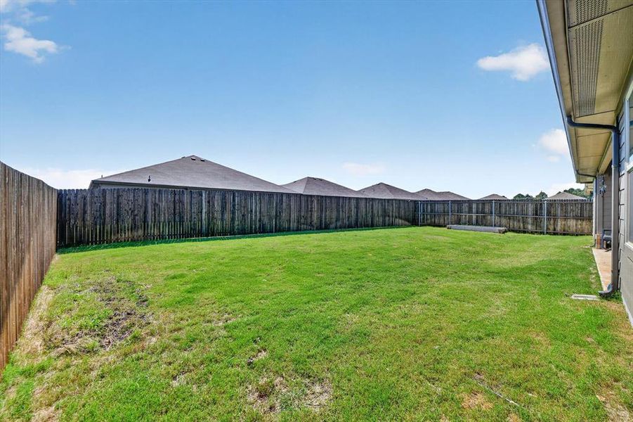 Expansive backyard featuring a lush green lawn, full privacy fencing, and a concrete patio area along the home's exterior