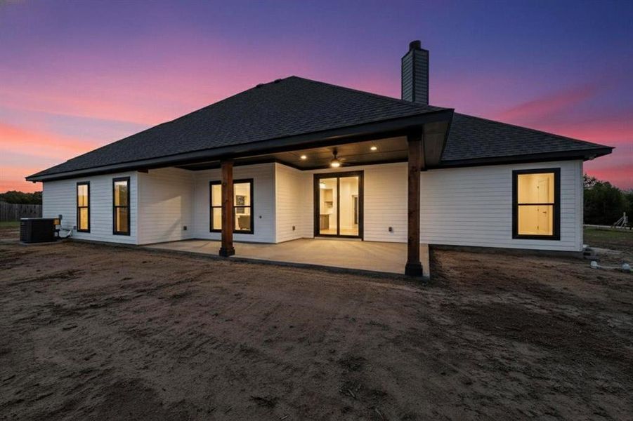 Back of property at dusk featuring a patio area, a shingled roof, and a chimney
