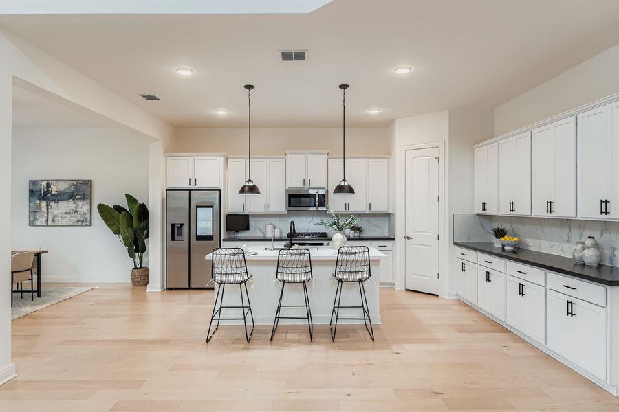 Kitchen with appliances with stainless steel finishes, hanging light fixtures, white cabinets, and an island with sink Kitchen with appliances with stainless steel finishes, hanging light fixtures, white cabinets, and an island with sink