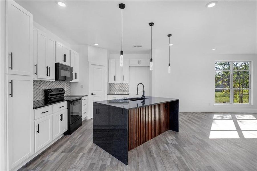 Kitchen featuring light hardwood / wood-style flooring, a center island with sink, decorative backsplash, white cabinets, and black appliances