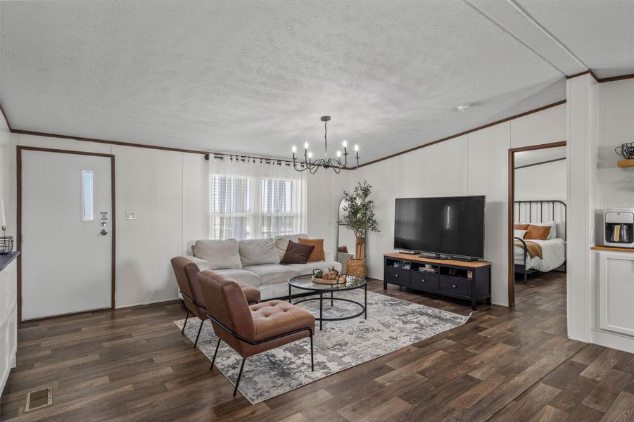 Living room with crown molding, a textured ceiling, dark wood-type flooring, and a chandelier