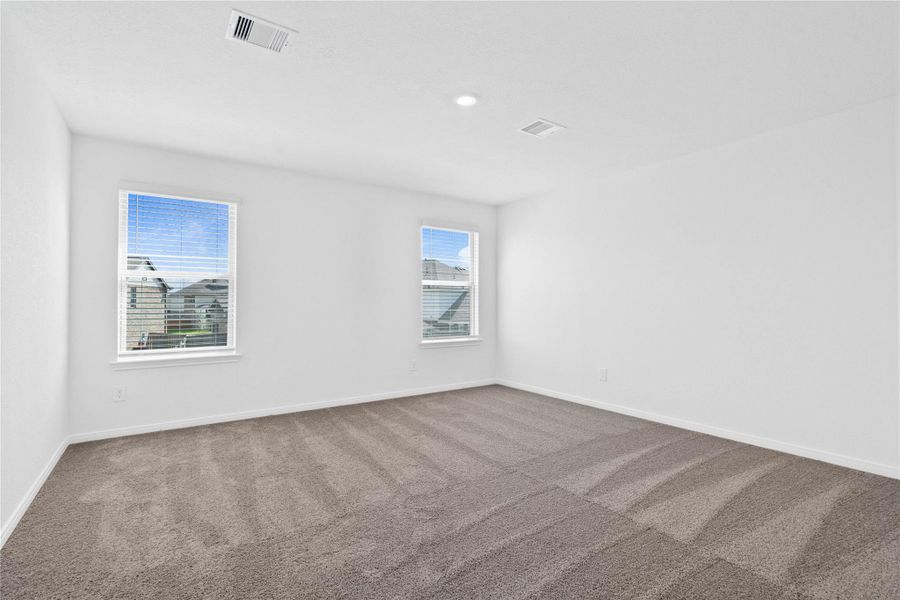 The stunning primary bedroom suite is a spacious retreat featuring plush carpeting, warm-toned walls, high ceilings, recessed lighting, and large windows with privacy blinds for comfort and tranquility.