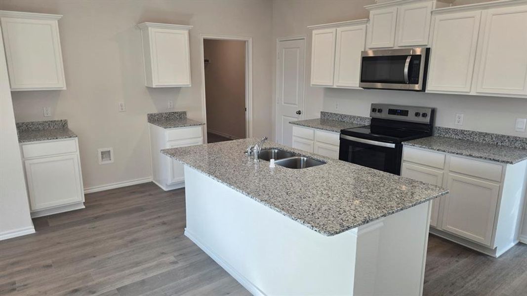 Kitchen featuring appliances with stainless steel finishes, white cabinetry, light stone counters, and dark wood finished floors