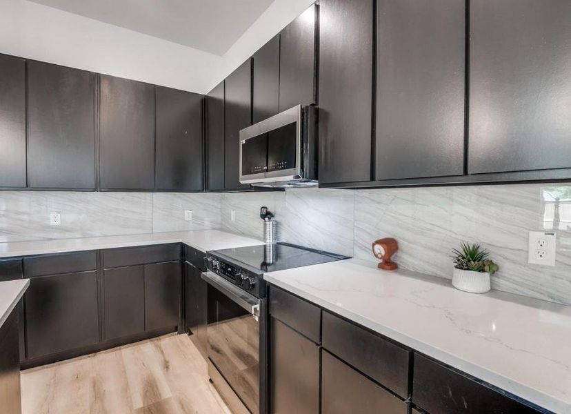 Kitchen with stainless steel appliances, decorative backsplash, light wood-type flooring, light stone countertops, and dark brown cabinetry