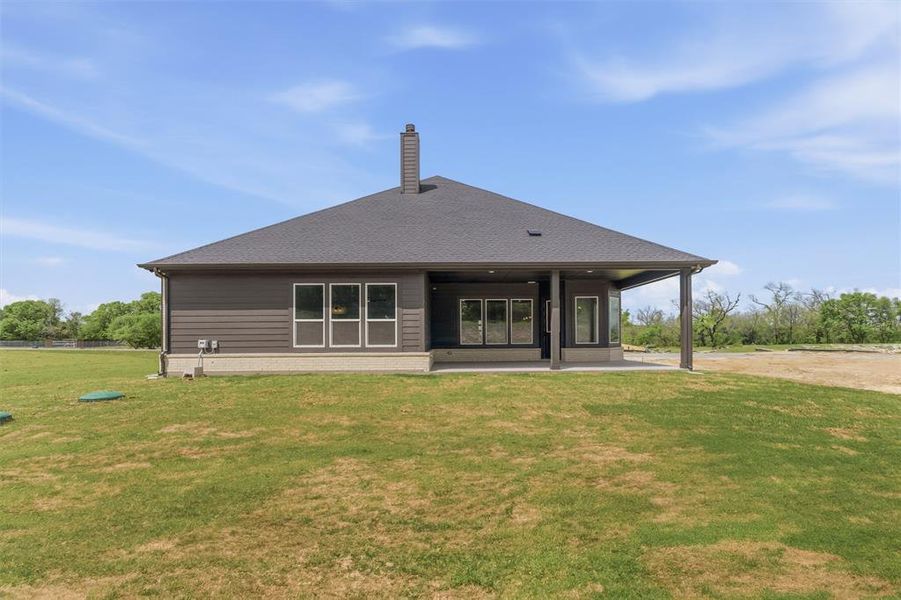 Rear view of house with a patio area, a lawn, a chimney, and a shingled roof