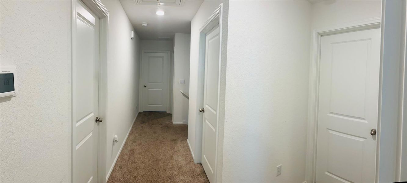 Carpeted hallway with multiple paneled doors and a wall-mounted thermostat Carpeted hallway with multiple paneled doors and a wall-mounted thermostat