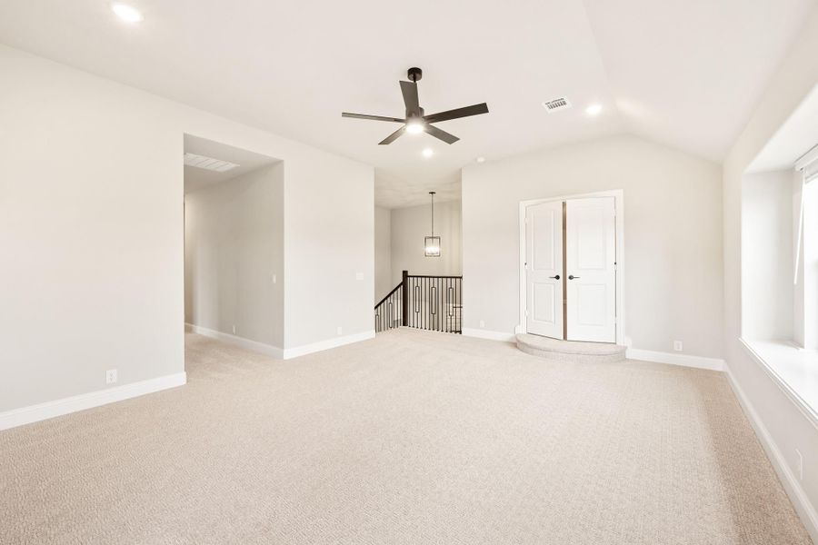 Spacious upstairs bonus room with carpet, ceiling fan, double doors, and staircase railing visible in background.