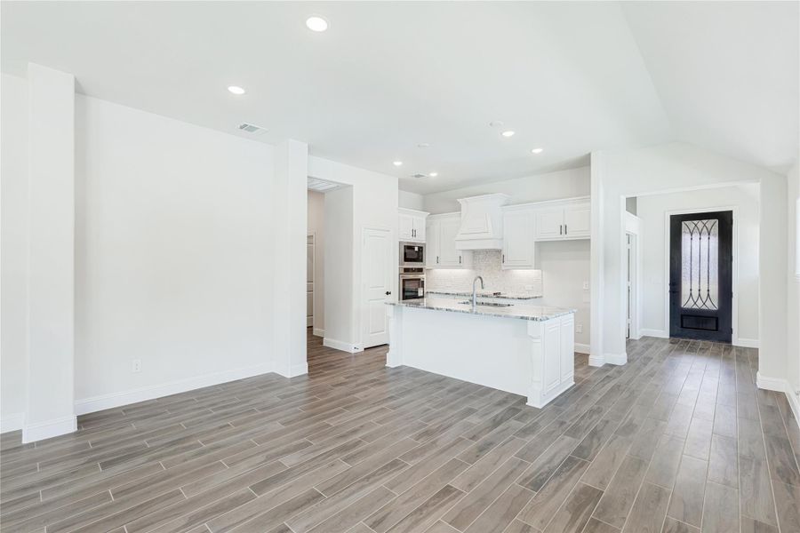 Open kitchen with white cabinets, center island, granite countertops, and wood-look tile floors Open kitchen with white cabinets, center island, granite countertops, and wood-look tile floors