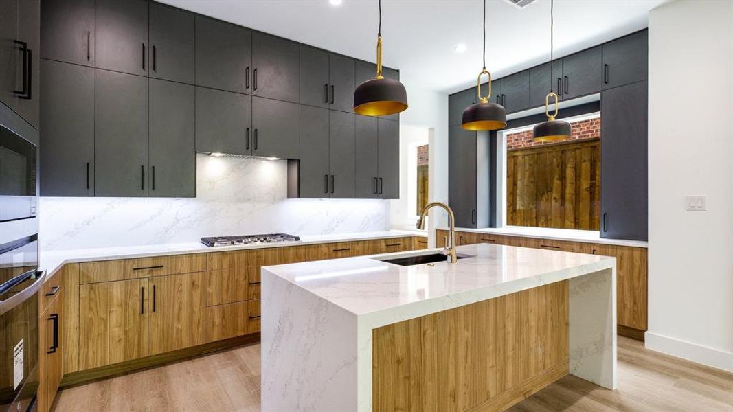 Kitchen featuring pendant lighting, a kitchen island with sink, light hardwood / wood-style flooring, decorative backsplash, and light stone counters