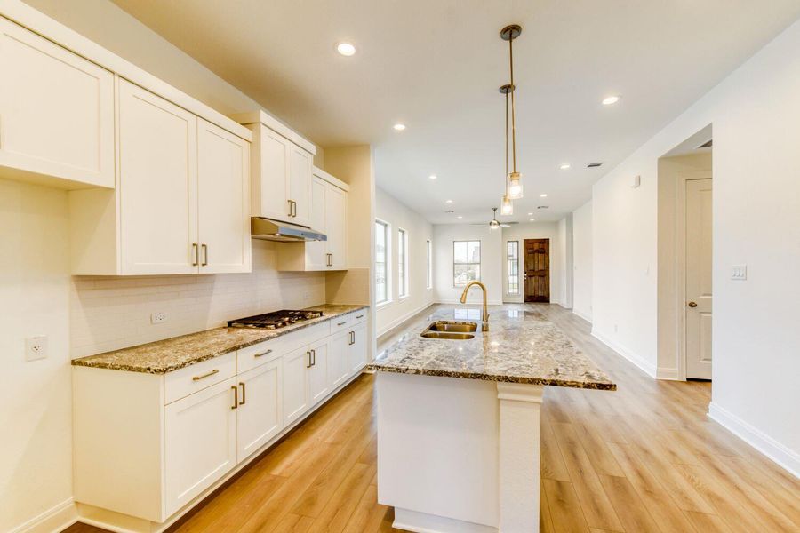 Kitchen featuring a kitchen island with sink, light stone countertops, white cabinetry, and light wood-type flooring