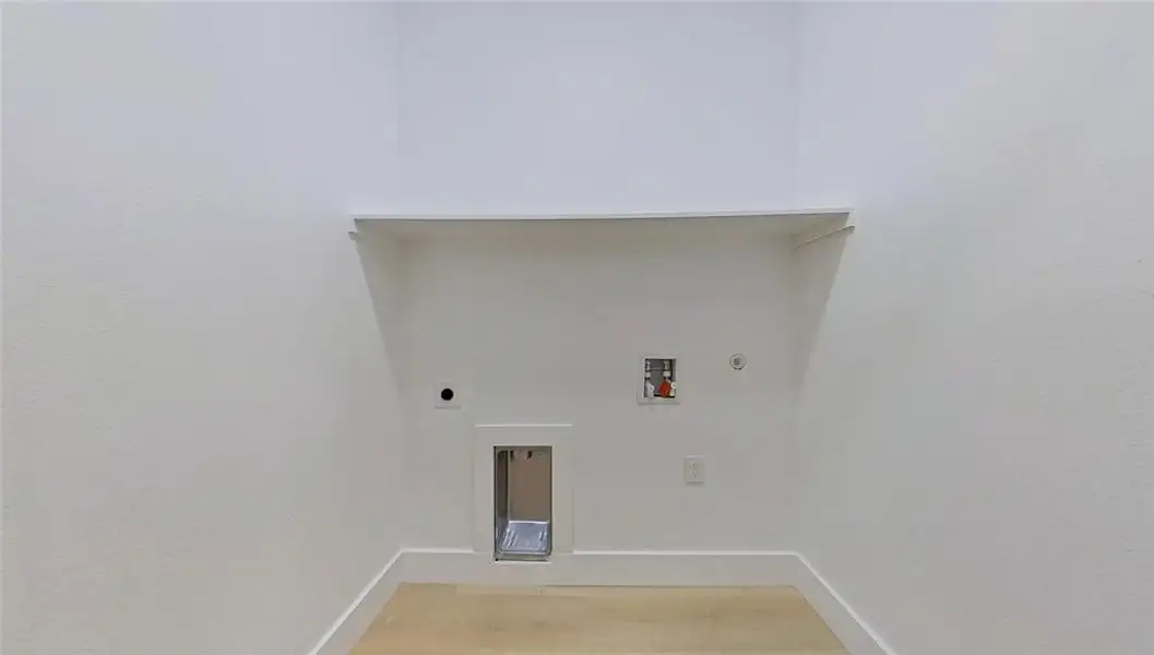 Dedicated laundry area with light wood-finish flooring, white walls, and a convenient overhead shelf