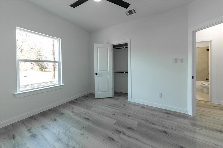 Unfurnished bedroom with ceiling fan, ensuite bath, a closet, and light hardwood / wood-style floors