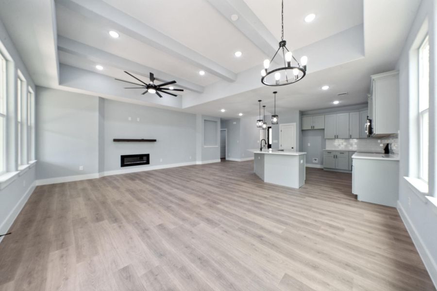 Spacious open-concept interior featuring light wood-finish flooring, a contemporary linear fireplace with a dark mantel, and vaulted ceilings with exposed beams