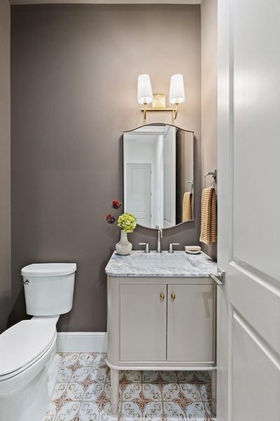 Elegant powder room featuring a chic vanity with marble counters and a patterned tile floor.