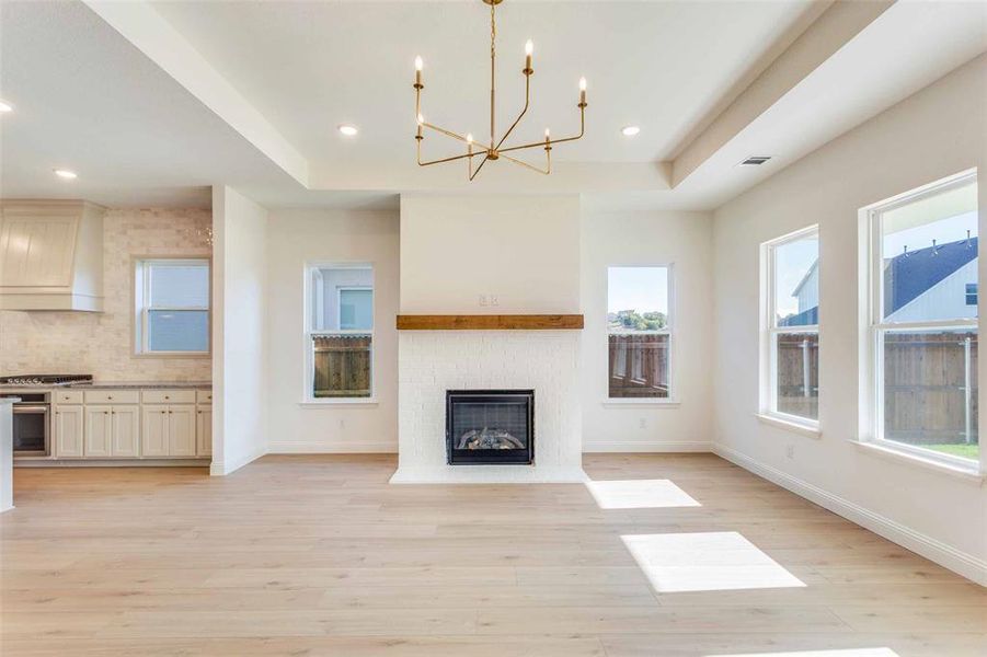 Unfurnished living room with a raised ceiling, light hardwood / wood-style flooring, a notable chandelier, and a brick fireplace