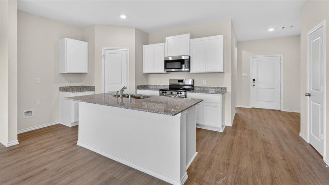 Modern kitchen featuring an island with a double basin sink, stainless steel appliances, white cabinetry, granite countertops, and wood-finish flooring